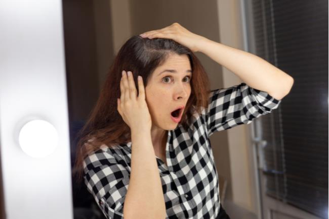 אישה צעירה מסתכלת במראה ומזועזעת מהשיער הלבן שצמח לה